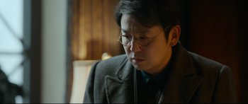 Movie still from “Cliff Walkers” (2021), directed by Yimou Zhang – A man wearing glasses and a jacket looking down; Close Up shot, Over the shoulder angle