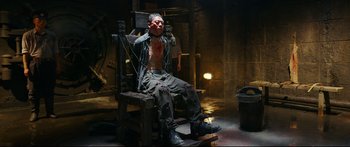 Movie still from “Cliff Walkers” (2021), directed by Yimou Zhang – A man sitting in a chair in a dark room; Medium shot, High angle