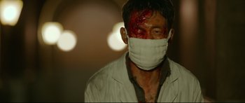 Movie still from “Cliff Walkers” (2021), directed by Yimou Zhang – A man wearing a surgical face mask with blood on his face; Medium shot, Low angle