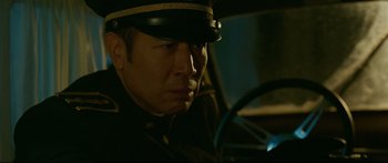 Movie still from “Cliff Walkers” (2021), directed by Yimou Zhang – A man wearing a hat sitting in the driver's seat of a car; Close Up shot, Low angle