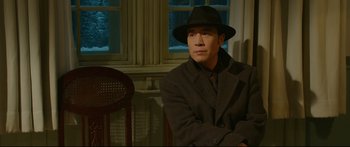 Movie still from “Cliff Walkers” (2021), directed by Yimou Zhang – A man wearing a hat and a suit sitting in a chair; Medium shot, Low angle