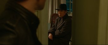Movie still from “Cliff Walkers” (2021), directed by Yimou Zhang – A man wearing a hat sitting on a chair; Medium shot, Over the shoulder angle