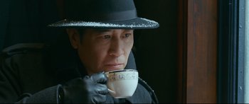 Movie still from “Cliff Walkers” (2021), directed by Yimou Zhang – A man wearing a hat and gloves holding a cup; Close Up shot, Low angle