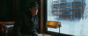 Movie still from “Cliff Walkers” (2021), directed by Yimou Zhang – A man sitting in front of a store window; Medium shot, Low angle