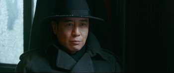 Movie still from “Cliff Walkers” (2021), directed by Yimou Zhang – A man wearing a hat and a black coat; Close Up shot, Low angle