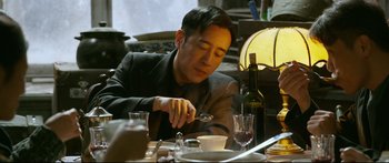 Movie still from “Cliff Walkers” (2021), directed by Yimou Zhang – A man sitting at a table with a bowl of food; Medium shot, Low angle