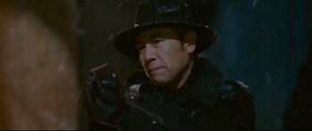 Movie still from “Cliff Walkers” (2021), directed by Yimou Zhang – A man wearing a hat and holding a gun in his hand; Close Up shot, Low angle