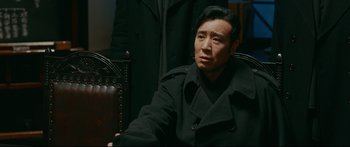 Movie still from “Cliff Walkers” (2021), directed by Yimou Zhang – A man sitting in a chair wearing a black coat; Close Up shot, Over the shoulder angle