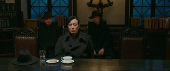 Movie still from “Cliff Walkers” (2021), directed by Yimou Zhang – A man sitting at a table with a cup of coffee; Medium shot, Over the shoulder angle
