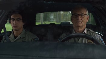 Movie still from “The Dead Don't Die” (2019), directed by Jim Jarmusch – A man driving a car with a man sitting in the passenger's seat; Close Up shot, Over the shoulder angle