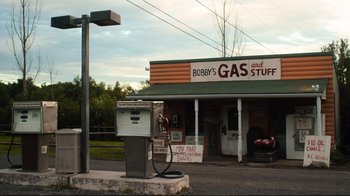 Movie still from “The Dead Don't Die” (2019), directed by Jim Jarmusch – An old gas station with a gas pump on the side of the road; Extreme Wide shot, High angle