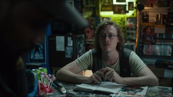 Movie still from “The Dead Don't Die” (2019), directed by Jim Jarmusch – A man sitting at a table with a book; Close Up shot, Over the shoulder angle