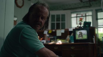 Movie still from “The Dead Don't Die” (2019), directed by Jim Jarmusch – A man sitting at a desk in front of a television; Close Up shot, Over the shoulder angle
