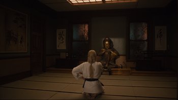 Movie still from “The Dead Don't Die” (2019), directed by Jim Jarmusch – A woman kneeling on the floor in front of a buddha statue; Wide shot, High angle