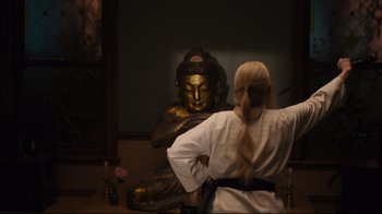 Movie still from “The Dead Don't Die” (2019), directed by Jim Jarmusch – A woman standing in front of a statue of a buddha; Medium shot, Over the shoulder angle