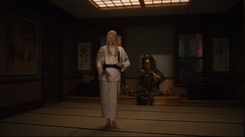 Movie still from “The Dead Don't Die” (2019), directed by Jim Jarmusch – A man in a white kimono stands in front of a buddha statue; Wide shot, High angle