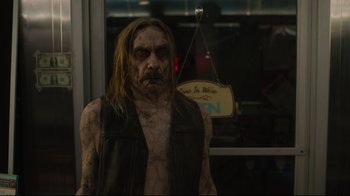 Movie still from “The Dead Don't Die” (2019), directed by Jim Jarmusch – A man with a long hair is standing in front of a store window; Medium shot, Over the shoulder angle