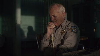 Movie still from “The Dead Don't Die” (2019), directed by Jim Jarmusch – A police officer talking on a phone while sitting down; Close Up shot, Low angle