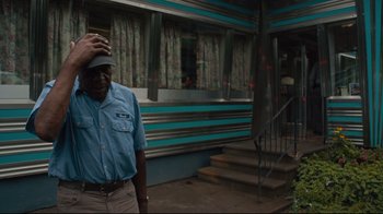 Movie still from “The Dead Don't Die” (2019), directed by Jim Jarmusch – A man standing in front of a building with his hand on his head; Medium shot, Low angle