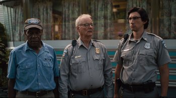 Movie still from “The Dead Don't Die” (2019), directed by Jim Jarmusch – A group of men standing next to each other in front of a building; Medium shot, Low angle
