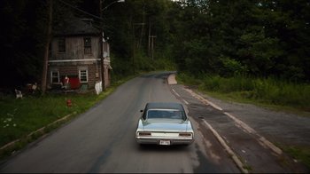 Movie still from “The Dead Don't Die” (2019), directed by Jim Jarmusch – A car driving down a road near some trees; Extreme Wide shot, High angle
