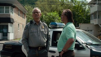 Movie still from “The Dead Don't Die” (2019), directed by Jim Jarmusch – Two men standing next to each other in front of a police car; Medium shot, Over the shoulder angle