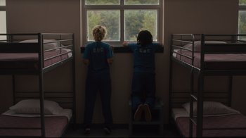 Movie still from “The Dead Don't Die” (2019), directed by Jim Jarmusch – Two people looking out a window in a room with bunk beds; Wide shot, Overhead angle