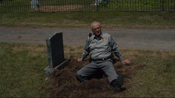Movie still from “The Dead Don't Die” (2019), directed by Jim Jarmusch – An old man sitting on the ground next to a grave; Wide shot, High angle