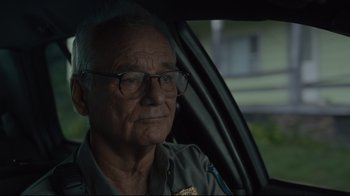 Movie still from “The Dead Don't Die” (2019), directed by Jim Jarmusch – An older man wearing glasses sitting in the driver's seat of a car; Close Up shot, Over the shoulder angle