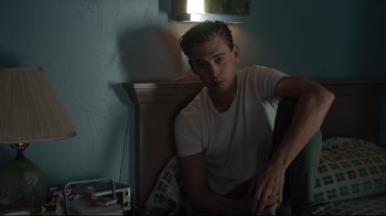 Movie still from “The Dead Don't Die” (2019), directed by Jim Jarmusch – A man sitting on top of a chair in a room; Medium shot, Low angle