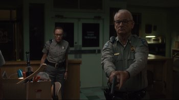 Movie still from “The Dead Don't Die” (2019), directed by Jim Jarmusch – A man and a woman standing in front of a building; Medium shot, Low angle