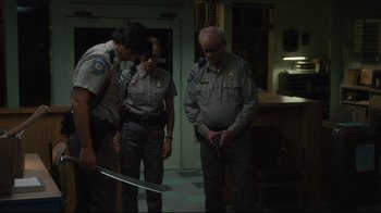 Movie still from “The Dead Don't Die” (2019), directed by Jim Jarmusch – A group of men standing around a room holding a knife; Medium shot, Over the shoulder angle