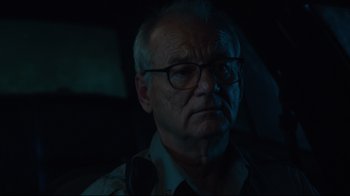 Movie still from “The Dead Don't Die” (2019), directed by Jim Jarmusch – An older man with glasses is sitting in a car; Close Up shot, Low angle