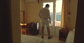 Movie still from “Climates” (2006), directed by Nuri Bilge Ceylan – A man standing in front of a window in a hotel room; Wide shot, High angle