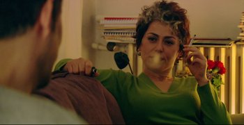 Movie still from “Climates” (2006), directed by Nuri Bilge Ceylan – A woman sitting on a couch smoking a cigarette; Medium shot, Over the shoulder angle