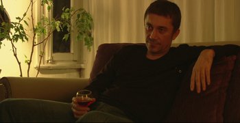 Movie still from “Climates” (2006), directed by Nuri Bilge Ceylan – A man sitting on a couch holding a glass of wine; Medium shot, Low angle