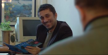 Movie still from “Climates” (2006), directed by Nuri Bilge Ceylan – A man sitting at a table holding a book; Medium shot, Over the shoulder angle