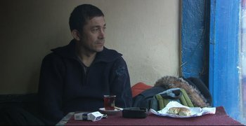 Movie still from “Climates” (2006), directed by Nuri Bilge Ceylan – A man sitting at a table with food on a plate; Medium shot, High angle