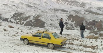 Movie still from “Climates” (2006), directed by Nuri Bilge Ceylan – A man standing next to a yellow car on a snowy hill; Extreme Wide shot, High angle