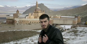 Movie still from “Climates” (2006), directed by Nuri Bilge Ceylan – A man in a leather jacket standing in front of a building; Medium shot, Low angle