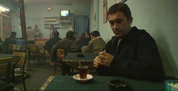 Movie still from “Climates” (2006), directed by Nuri Bilge Ceylan – A man sitting at a table with a cup of tea; Medium shot, High angle
