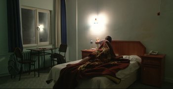 Movie still from “Climates” (2006), directed by Nuri Bilge Ceylan – A person sitting on a bed in a hotel room; Medium shot, High angle