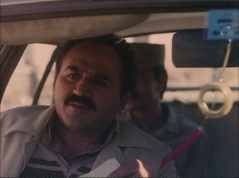 Movie still from “Close-Up” (1990), directed by Abbas Kiarostami – A man driving a car while another man holds a pen in his hand; Close Up shot, Low angle