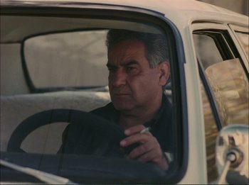 Movie still from “Close-Up” (1990), directed by Abbas Kiarostami – A man sitting in the driver's seat of a white car; Close Up shot, Over the shoulder angle