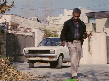 Movie still from “Close-Up” (1990), directed by Abbas Kiarostami – A man walking down the street in front of an old car; Wide shot, Low angle