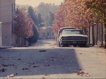 Movie still from “Close-Up” (1990), directed by Abbas Kiarostami – A car parked on the side of the street; Extreme Wide shot, High angle