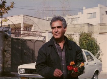 Movie still from “Close-Up” (1990), directed by Abbas Kiarostami – An older man holding a bouquet of flowers; Medium shot, Low angle