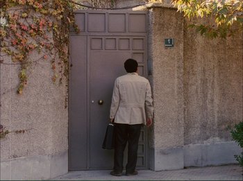 Movie still from “Close-Up” (1990), directed by Abbas Kiarostami – A man with a briefcase standing in front of an open door; Wide shot, High angle