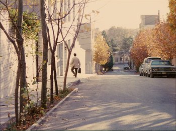 Movie still from “Close-Up” (1990), directed by Abbas Kiarostami – A man riding down the side of a street with a suitcase; Extreme Wide shot, High angle