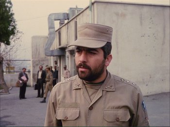 Movie still from “Close-Up” (1990), directed by Abbas Kiarostami – A man in a military uniform standing in front of a group of people; Close Up shot, Over the shoulder angle